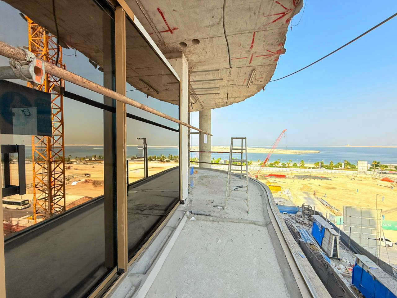 Beach Walk Iii By Imtiaz A construction site view featuring a balcony with scaffolding, overlooking a shoreline and building materials.